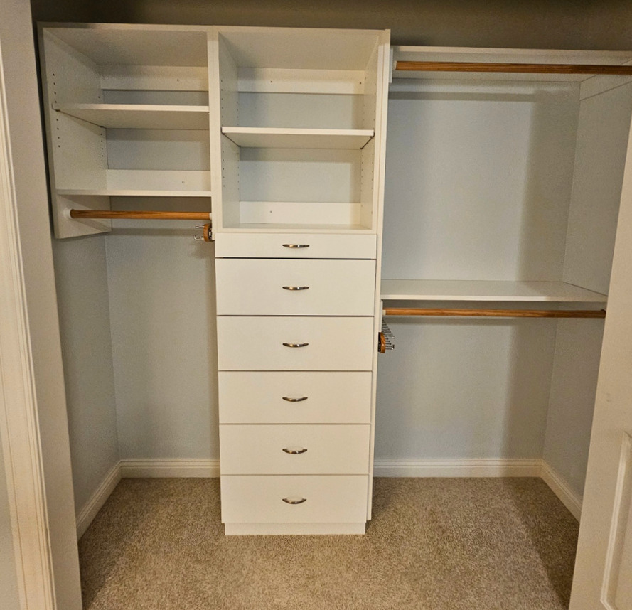 A custom closet build-out with shelving, drawers, and hanging rods
